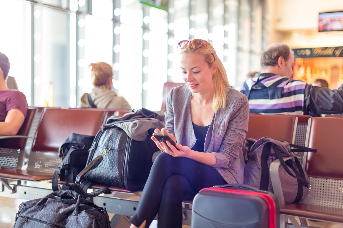 A smiling woman uses Wi-Fi in an airport thanks to high-density Wi-Fi design principles.