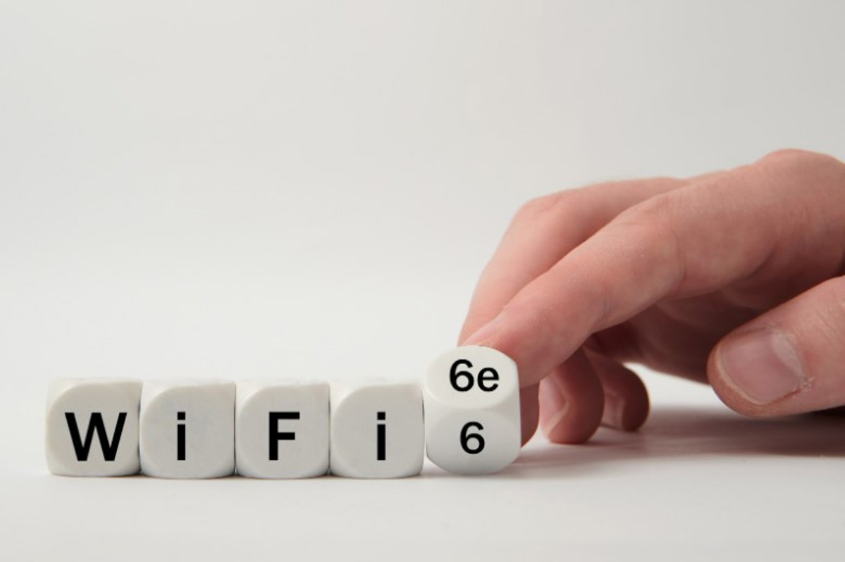 A set of dice spell out Wi-Fi 6 with a hand flipping the last die over to read 6E